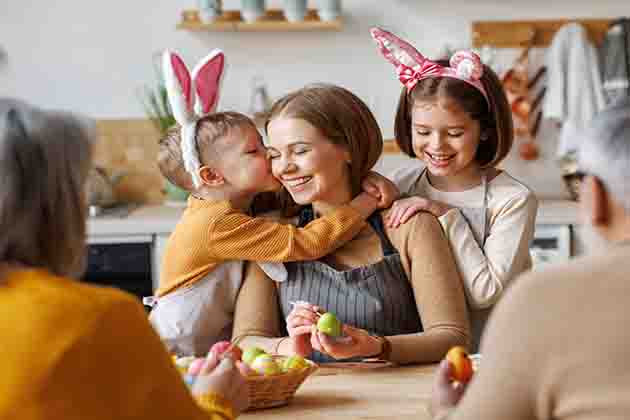 Três adultos e duas crianças com orelhas de coelho em volta de uma mesa. O menino está beijando o rosto de uma mulher.