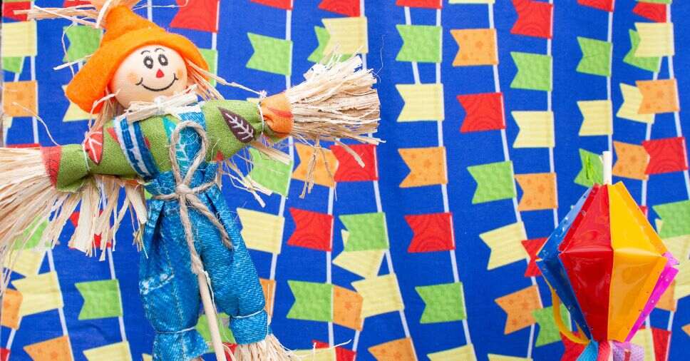 Boneco de espantalho e balão colorido em fundo decorado ilustram festa junina em condomínio.