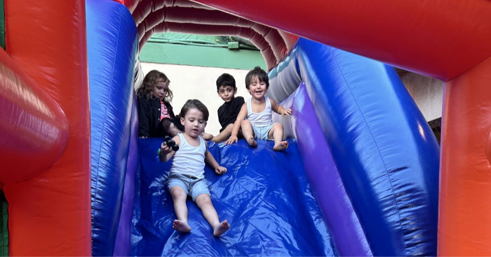 Crianças descendo brinquedo inflável em lazer, estimulando as habilidades sociais na infância.
